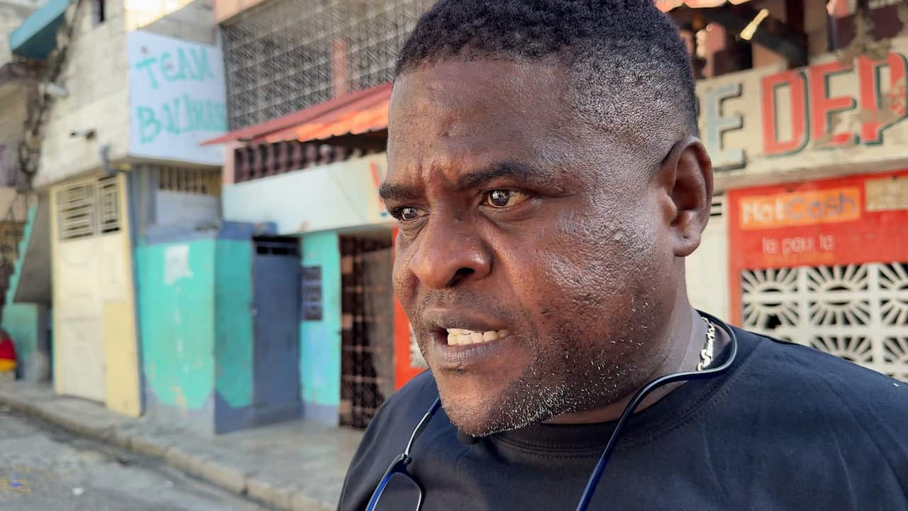 A close-up shot of a Black man’s face, wearing a black t-shirt and headphones hanging around his neck