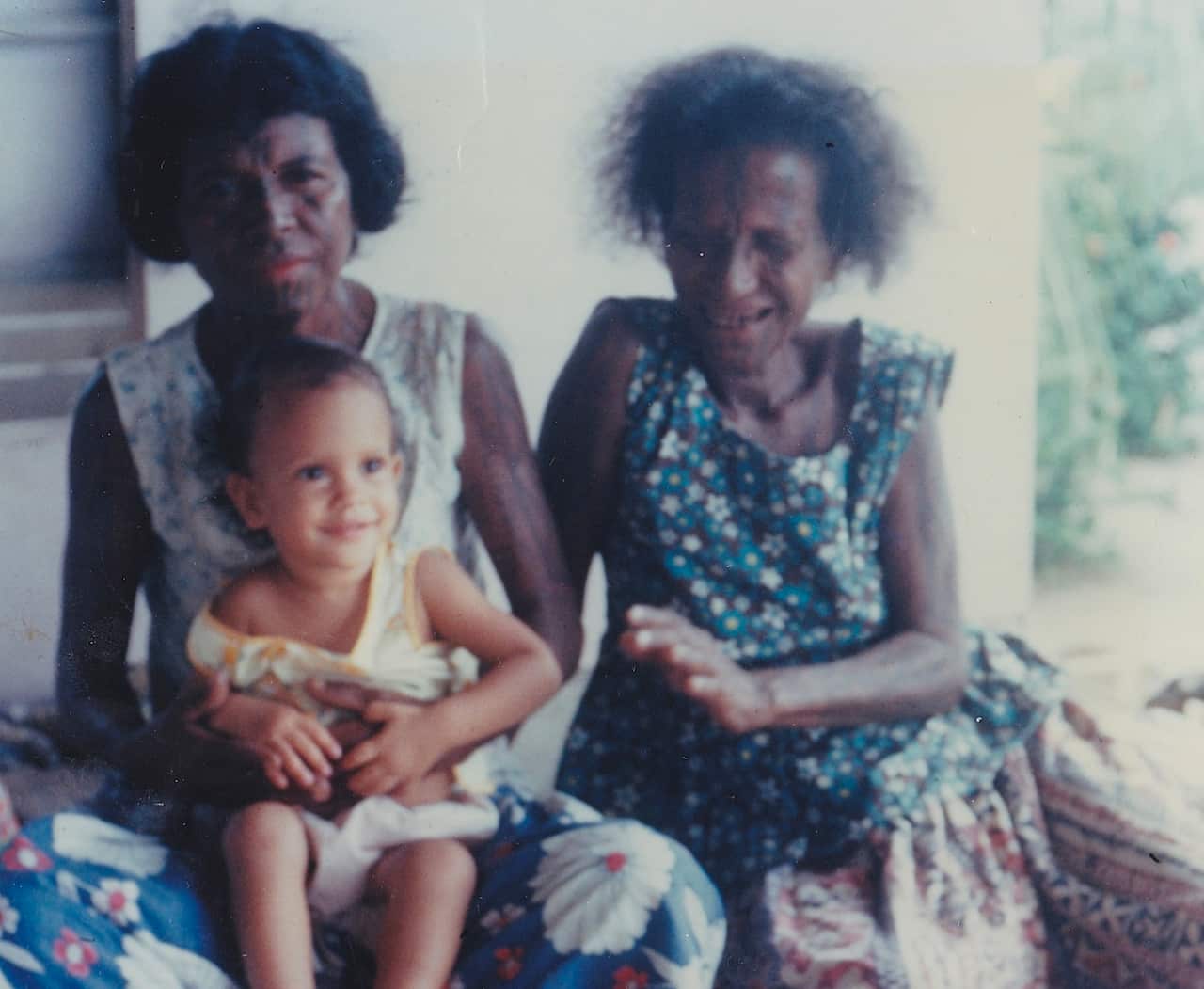Two women with facial markings and a baby sitting 