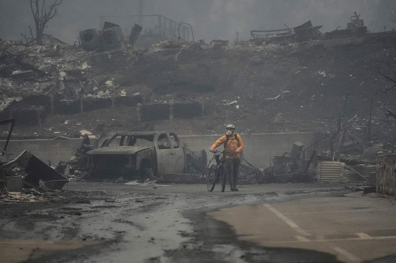 A man with a bike is standing in a street surrounded by burnt cars and buildings.