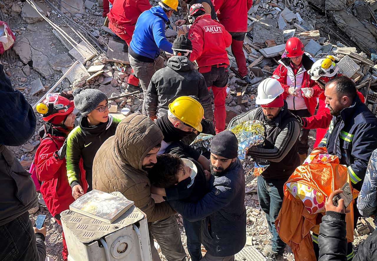 Some rescue workers inspect an area while others are seen carrying a child.