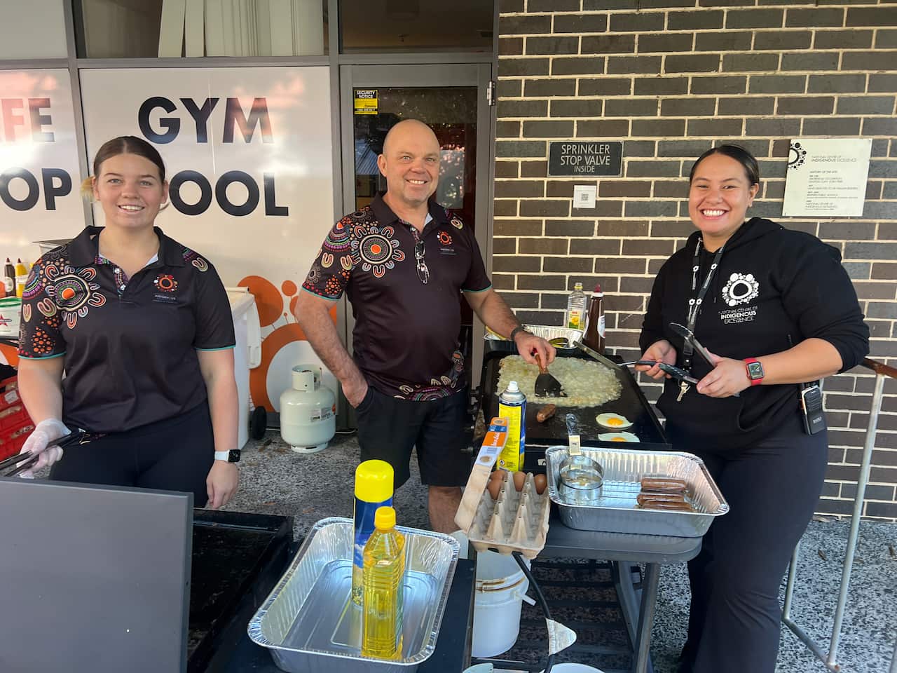 Three people manning a barbecue.