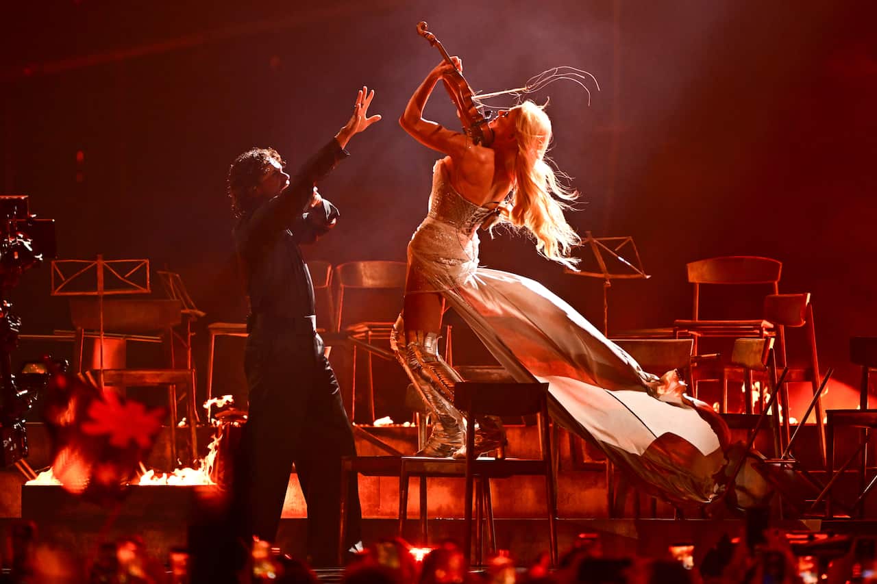 A performer plays a violin on a stage with another performer raising his hand