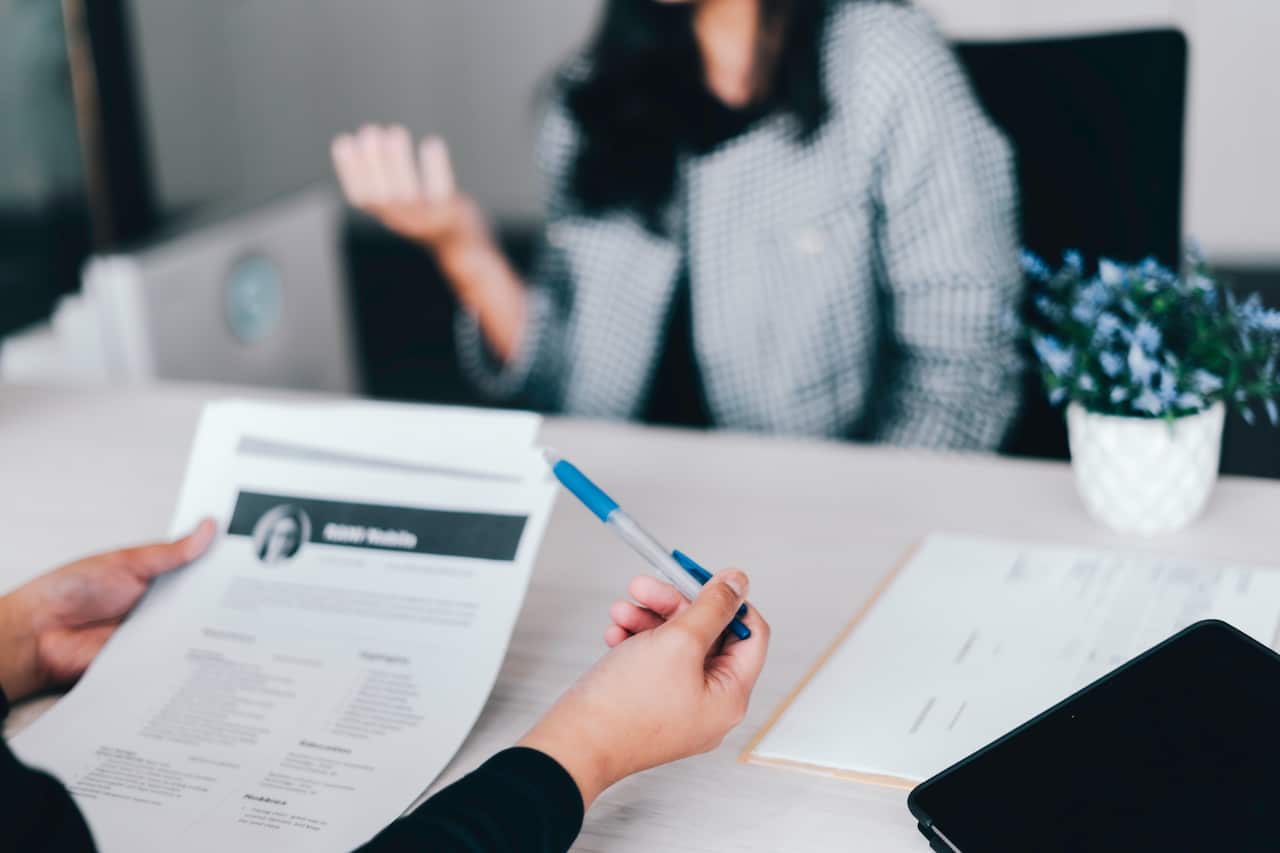A woman at a desk across from someone holding a resume in front of them.