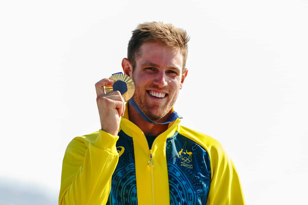 A man wearing a green-and-gold tracksuit holds up a gold medal