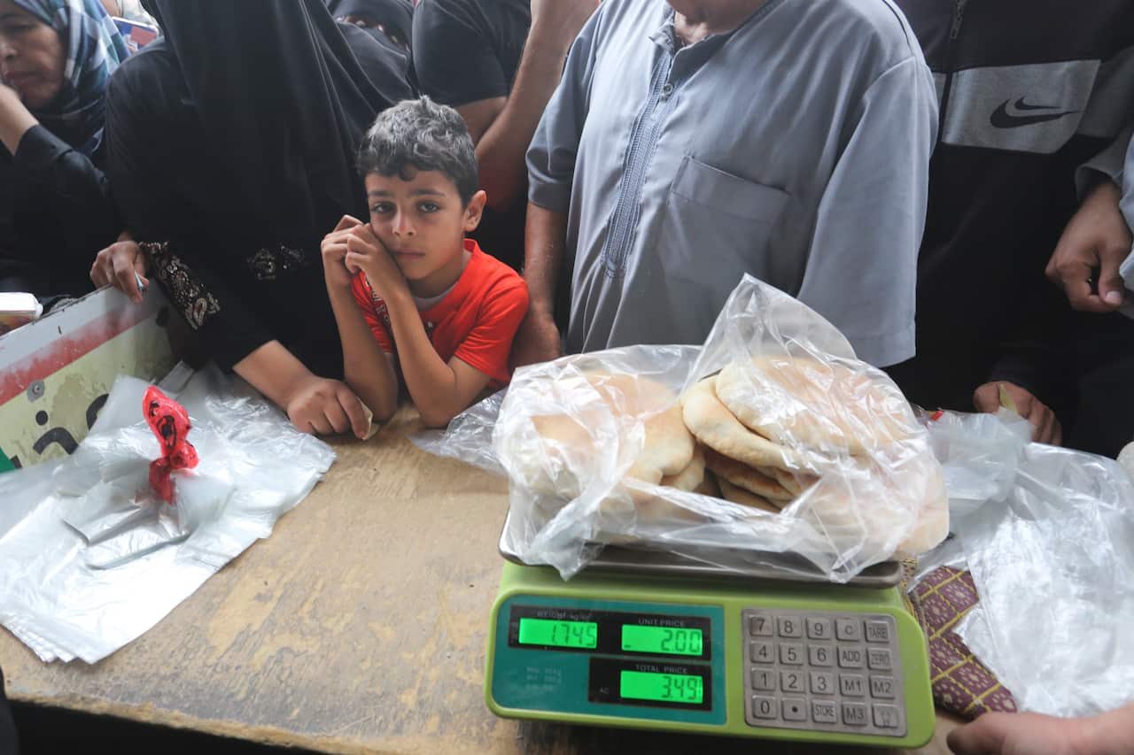 A child leans on a counter with scales and bread on it.