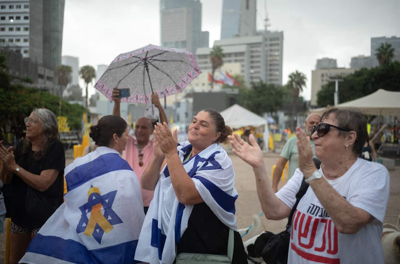 A group of women, some with Israeli flags draped over their bodies, clap their hands in celebration