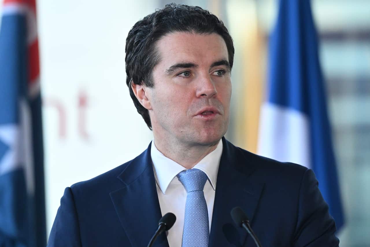 A man with black curly hair in a suit speaking.