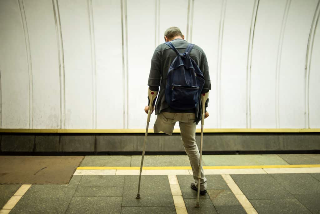 A rear view of a man with an amputated leg standing with crutches.