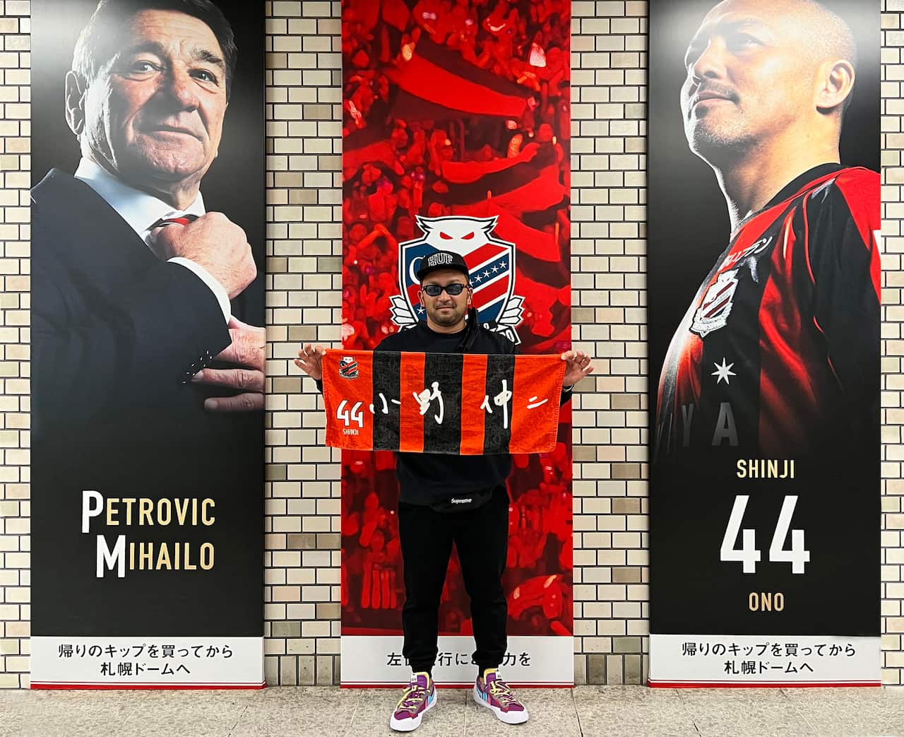 Yasuke Oba holding a red and white flag and standing in front of sporting posters.