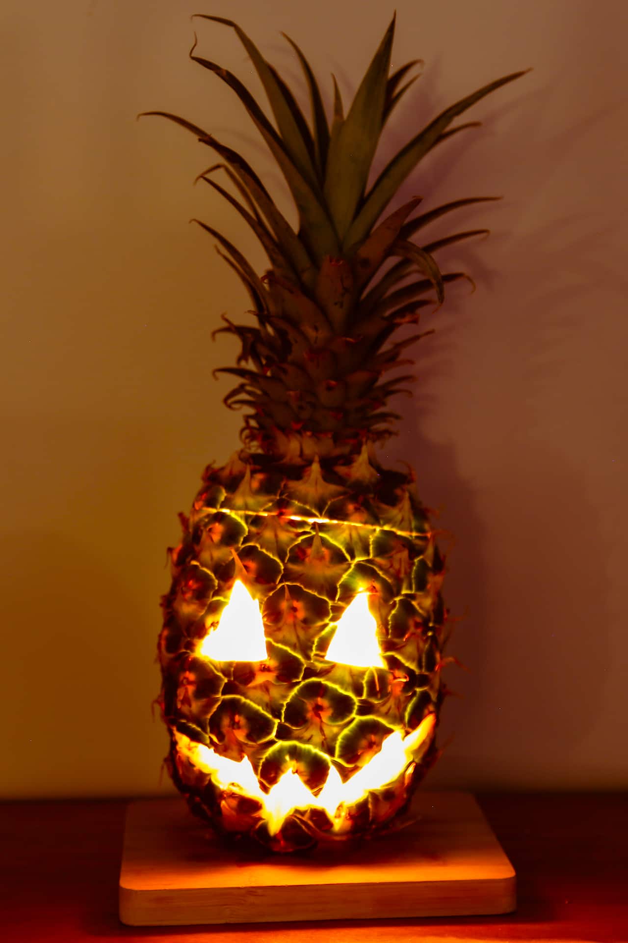 A pineapple with a face carved in it, its top cut but placed back on top and light shining from within it.