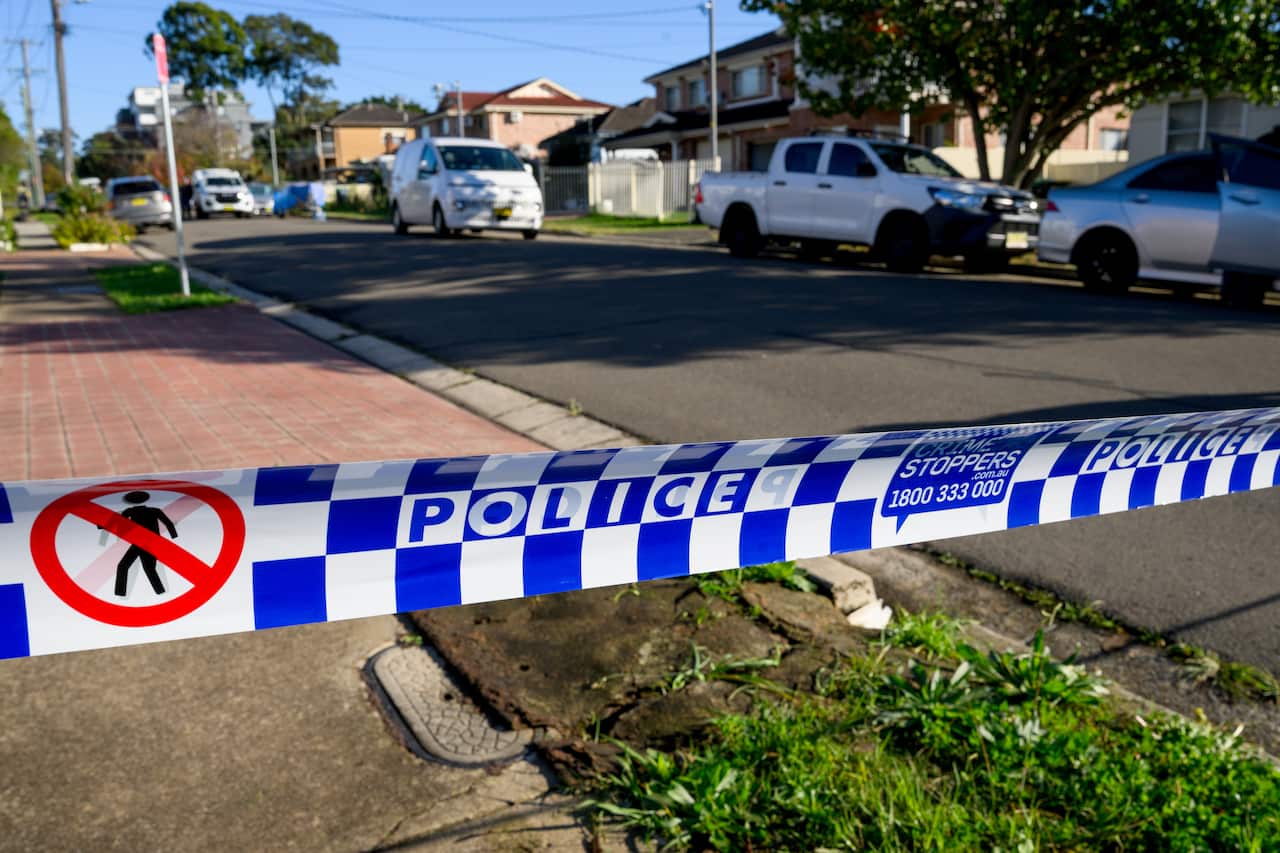 Police tape marks out a crime scene outside homes in a suburban street.
