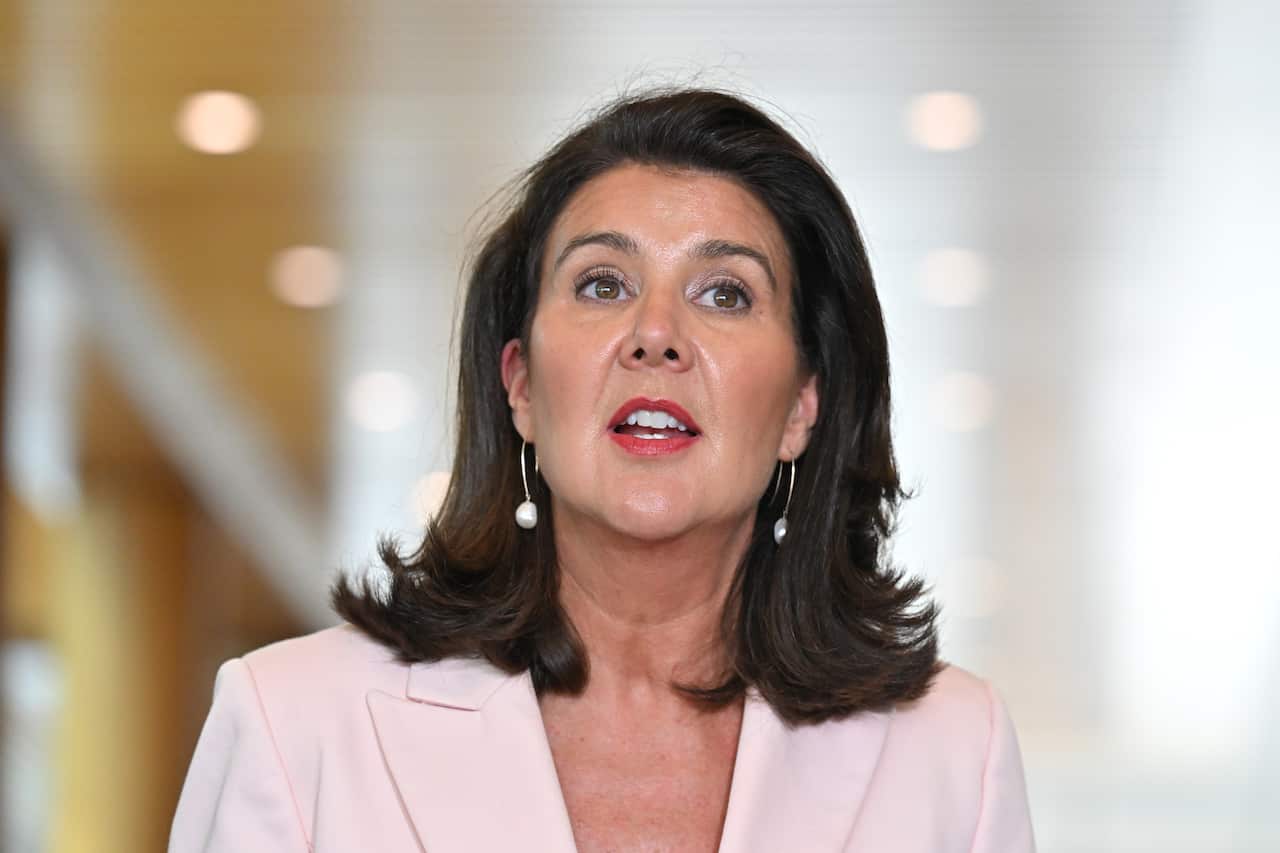 A woman with shoulder length dark hair and wearing a light pink jacket is talking