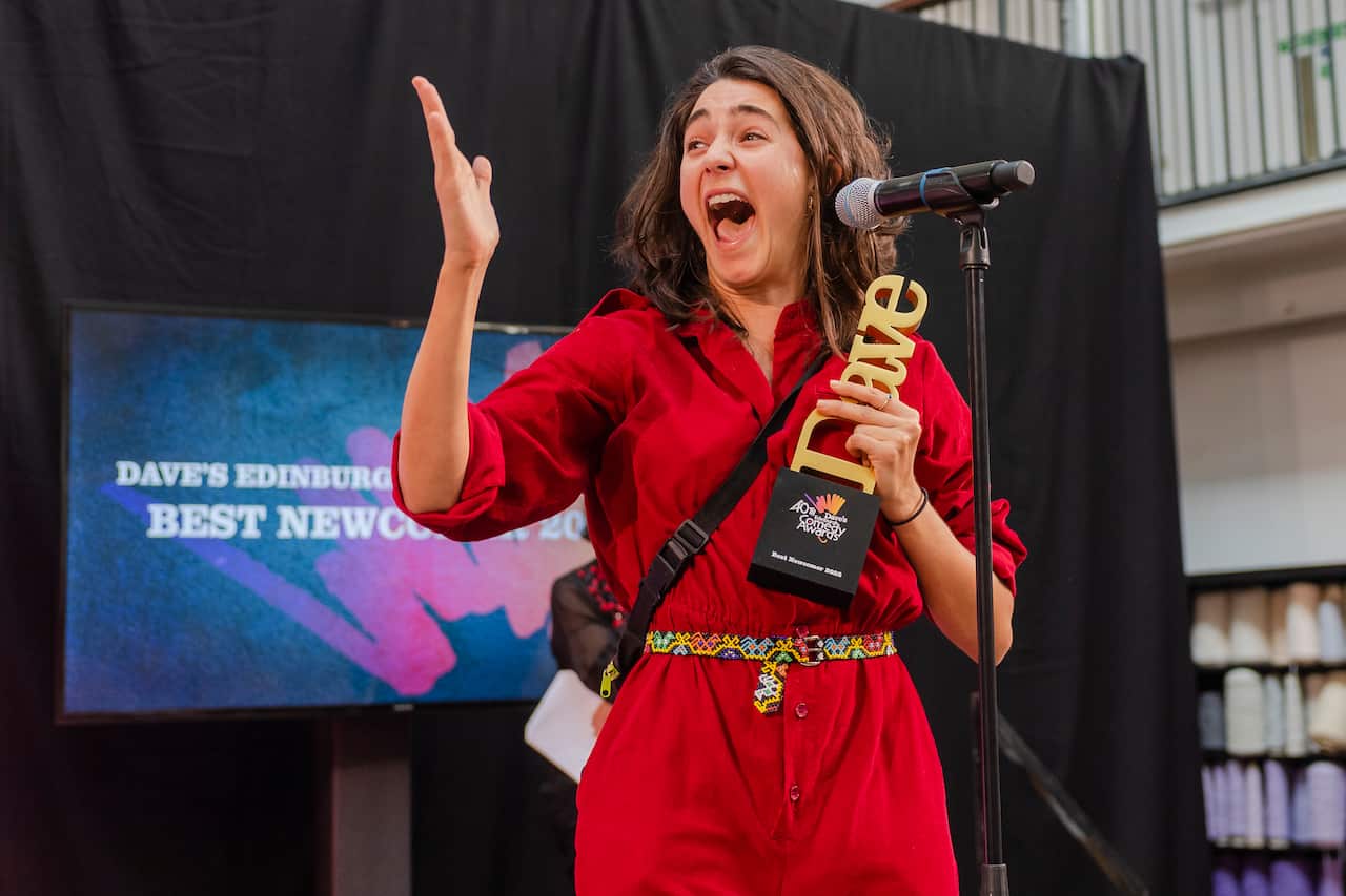 A woman in a red jumpsuit standing behind a microphone and holding an award