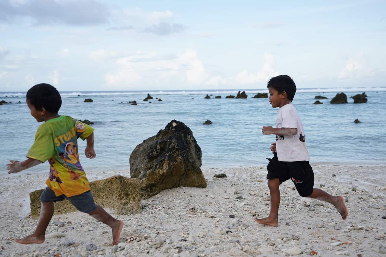 Two kids run on a beach