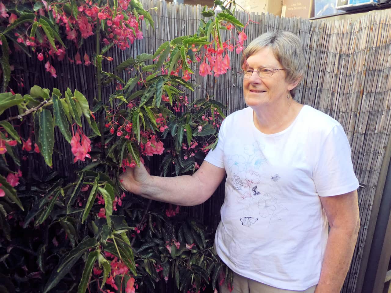 A woman wearing a white t-shirt and glasses standing next to flowers 