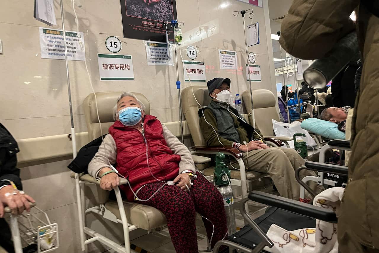 An elderly woman sits with a face mask and IV drip in a Chinese hospital