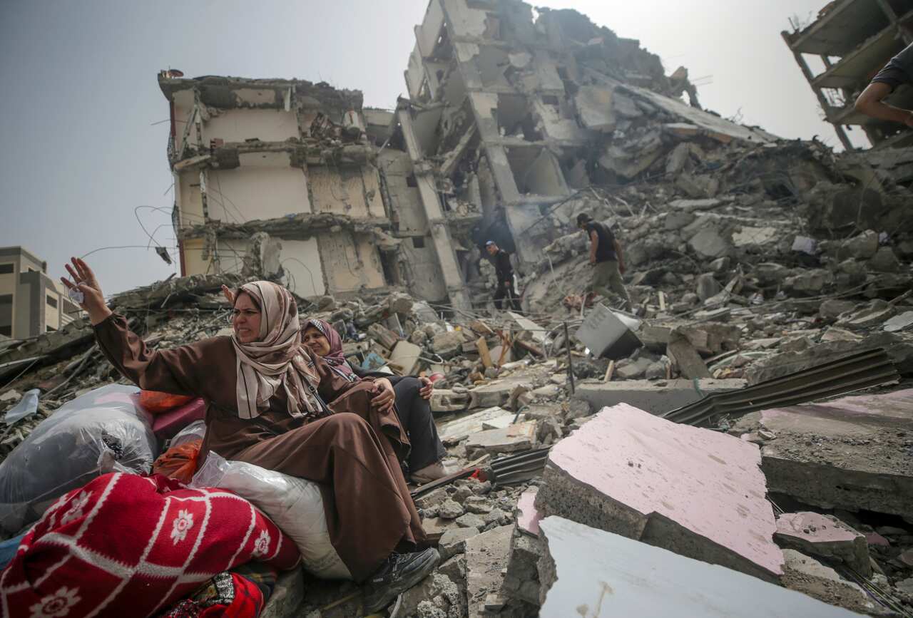 Women sit in rubble of a building.