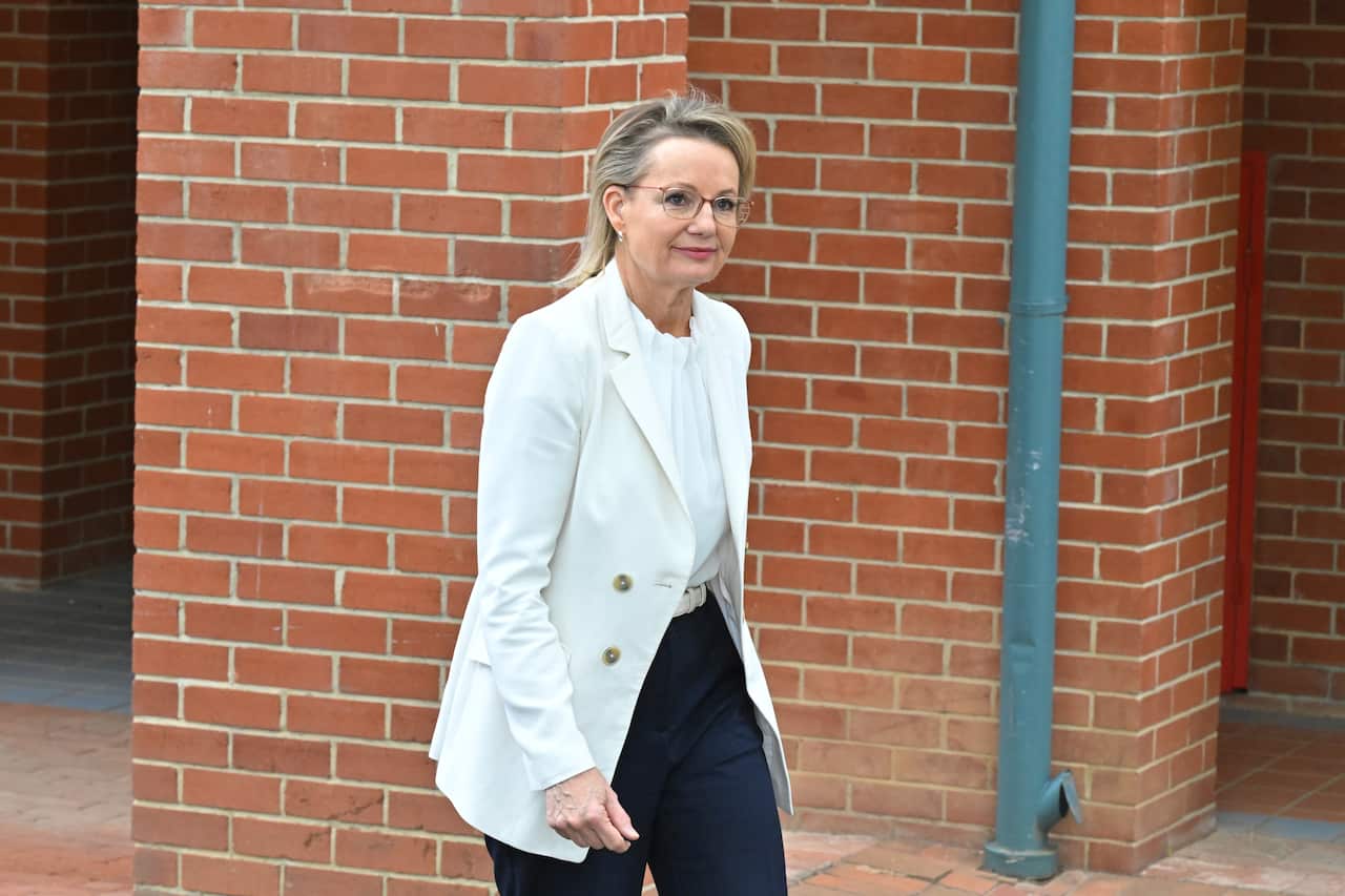 A woman in a white suit jacket walks outside smiling