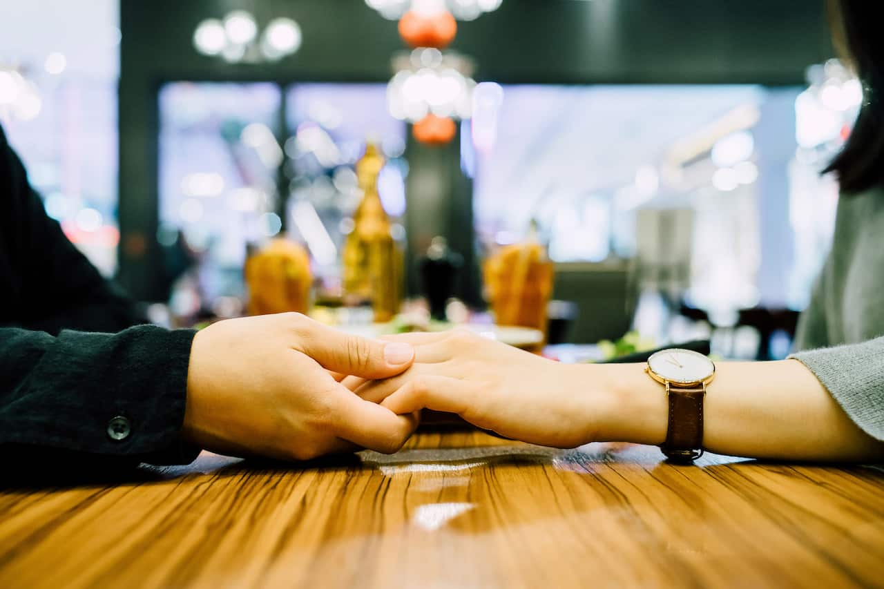 Hai người trẻ nắm tay nhau trong một buổi ăn tối ở nhà hàng