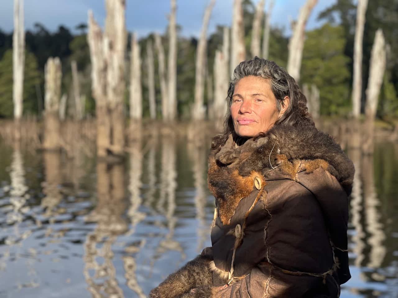 A woman wearing a possum coat stares out across the water.