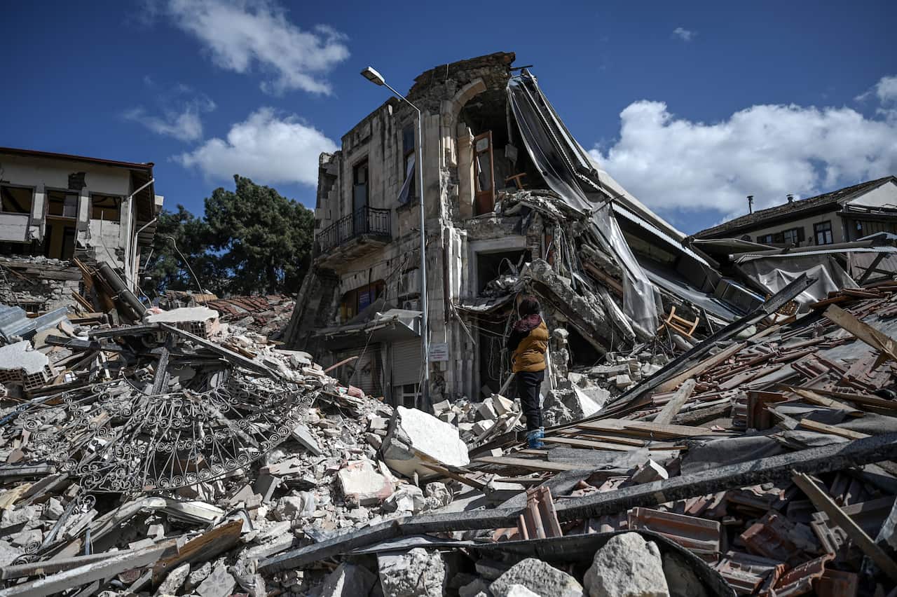 A woman stands among the rubble of collapsed buildings.
