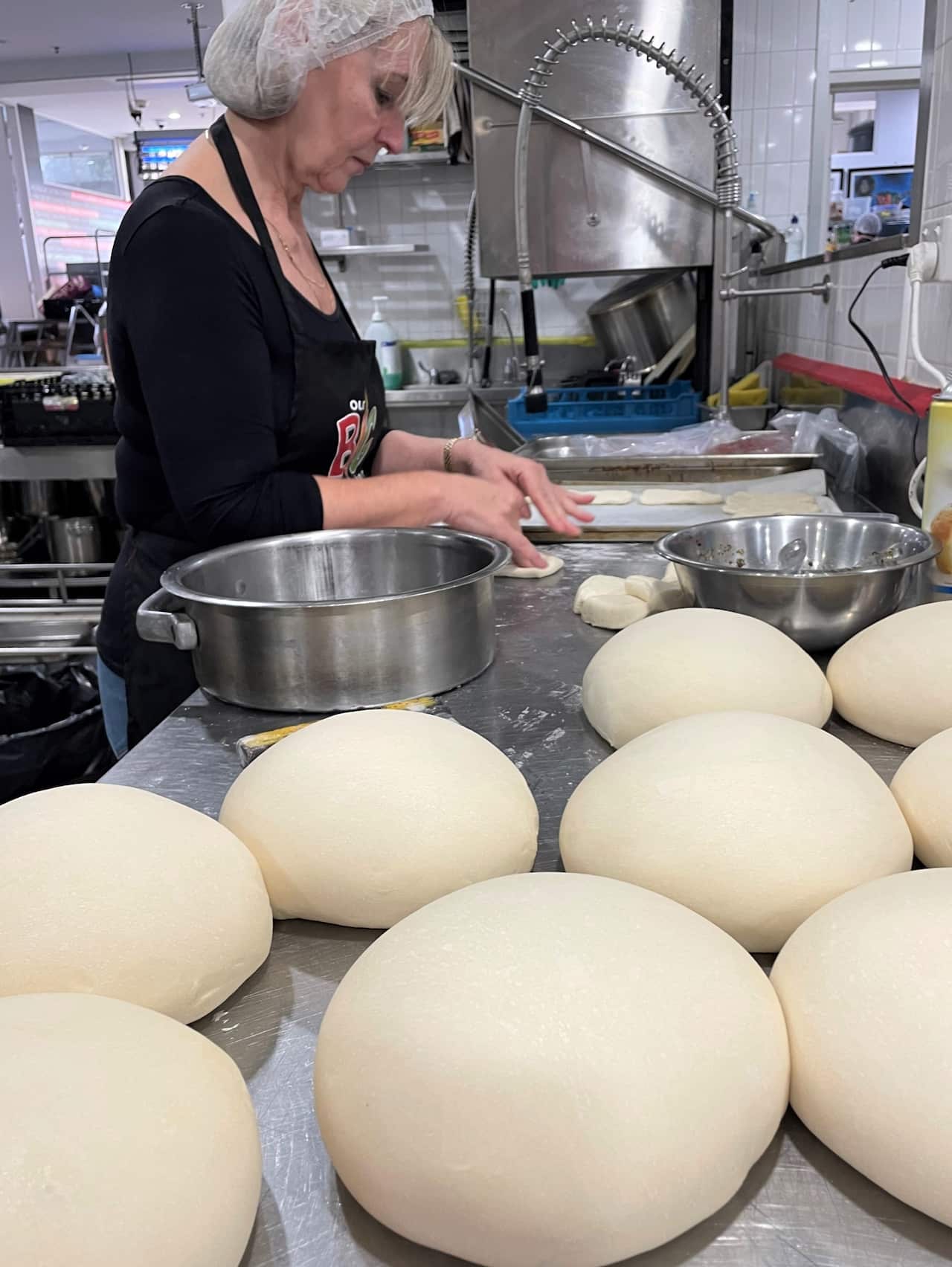 A woman in a hairnet stands at a counter beside mounds of unbaked bread.