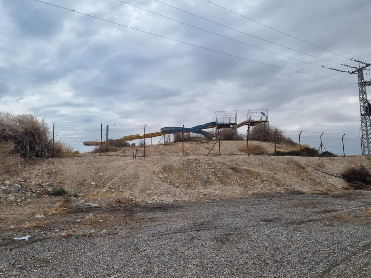 An abandoned water slide on a mound of yellowish dirt behind a barbed-wire fence.