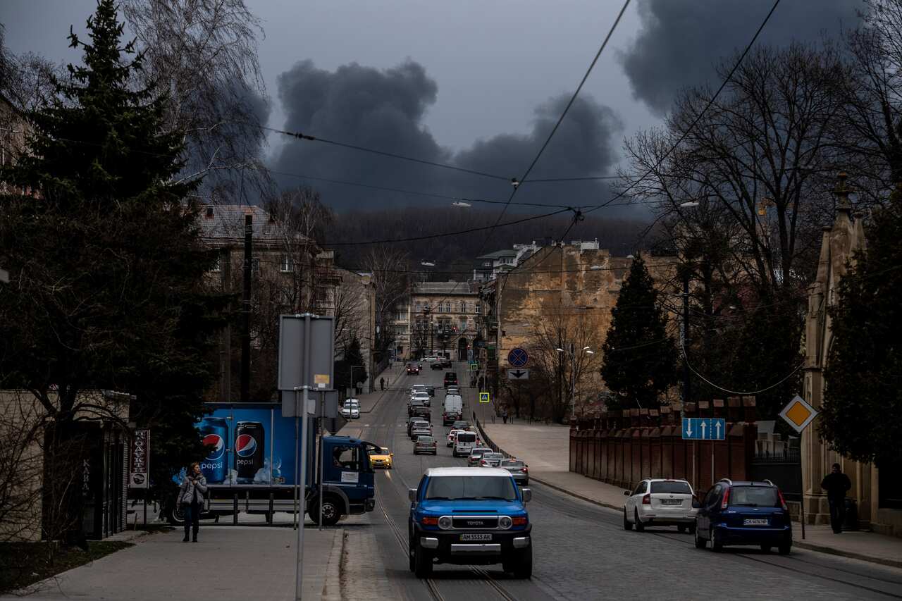 Cares are seen driving along a street as smoke is seen in the background.