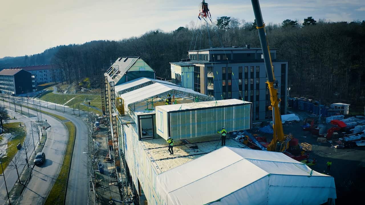 A construction site for a residential building, with a crane lifting modular blocks and construction workers working around the site