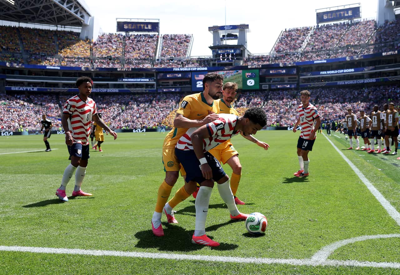 A footballer in a red and white striped jersey and dark blue shorts shields the ball near the corner as a player in all-yellow kit pushes against him