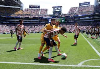 A footballer in a red and white striped jersey and dark blue shorts shields the ball near the corner as a player in all-yellow kit pushes against him