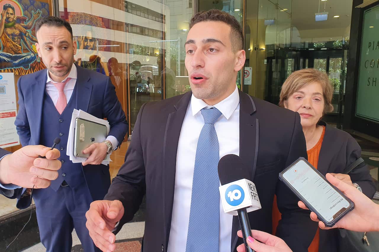 A man in a suit and tie speaking in front of microphones.
