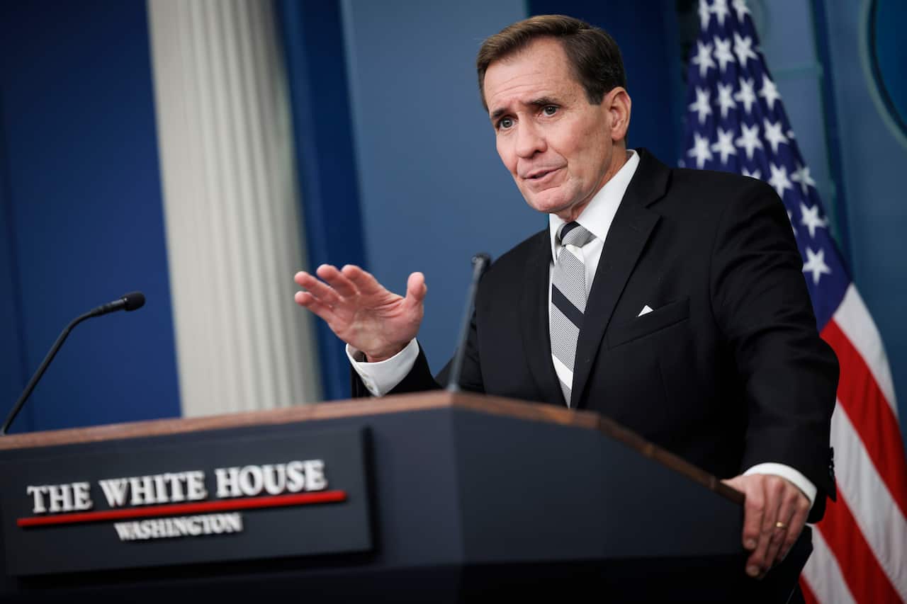 A middle-aged man wearing a black suit and grey tie speaks at a lectern. 