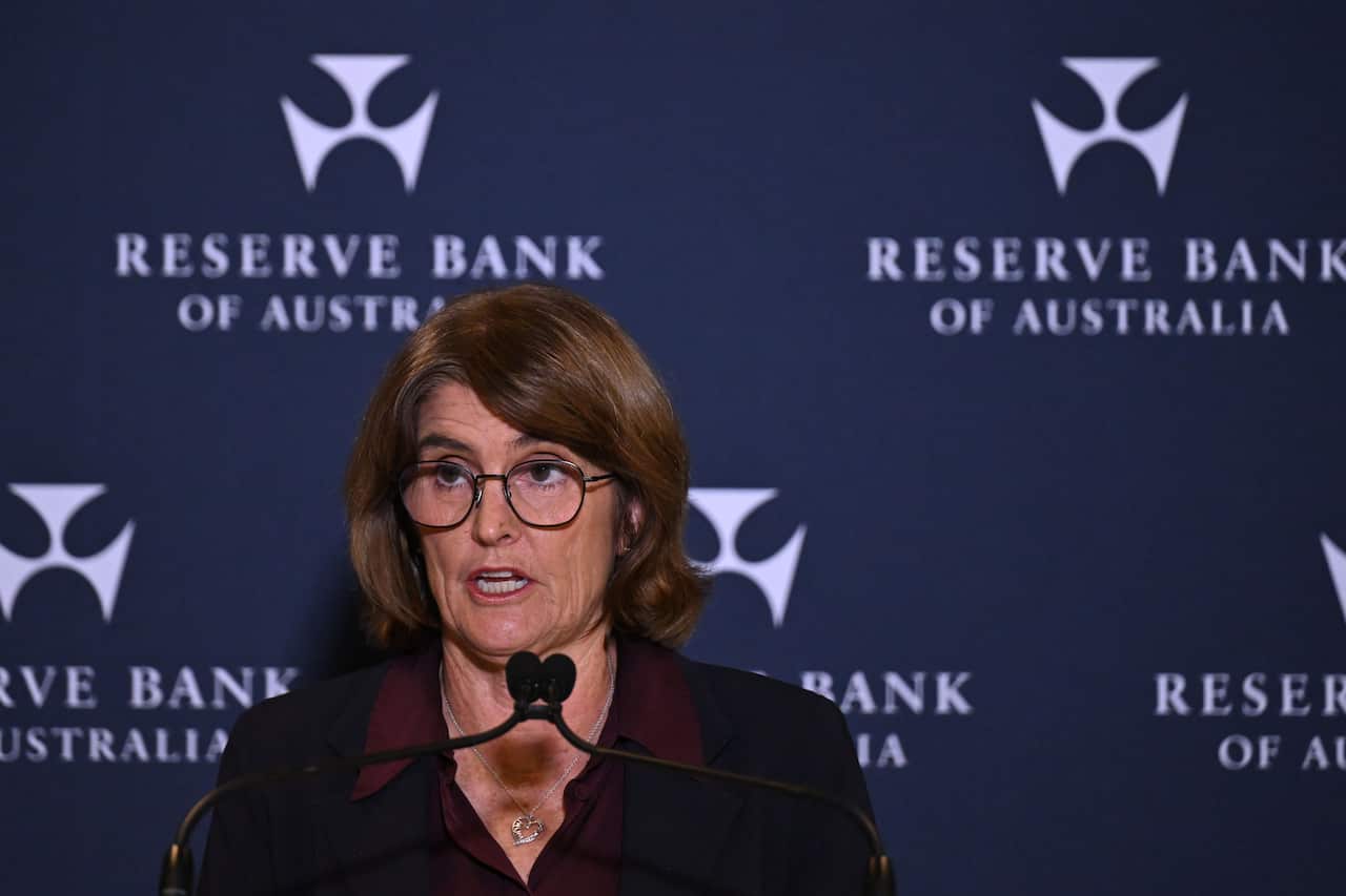 Michele Bullock speaking into a microphone. There is a blue wall behind her with the Reserve Bank of Australia logo.