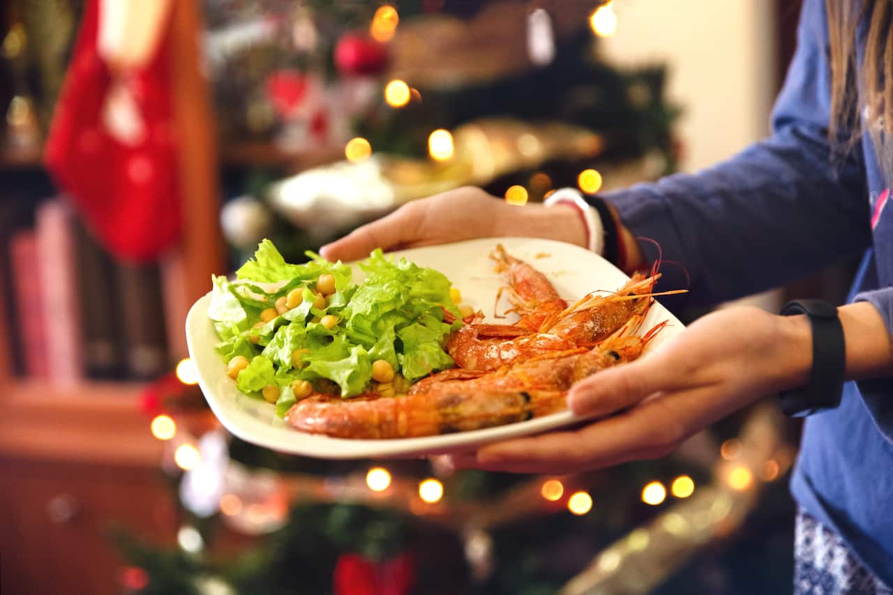 Close-up of a plate with salad and prawns held in the hand of a teenage girl who brings it to the Christmas table. Behind you see the bokeh of the Christmas tree lights