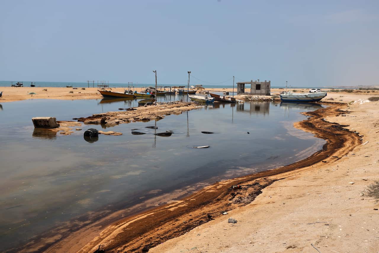 Oil residue lines a desert shore with boats visible in the background.