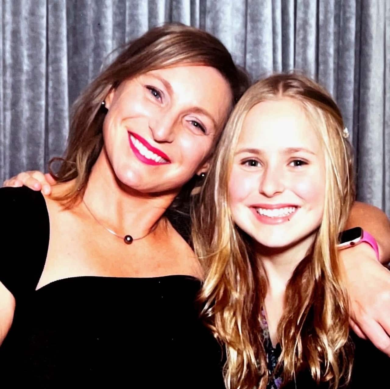 A photo of a smiling woman with brown hair wearing a black dress with her arm around a smiling teenage girl with blonde hair.