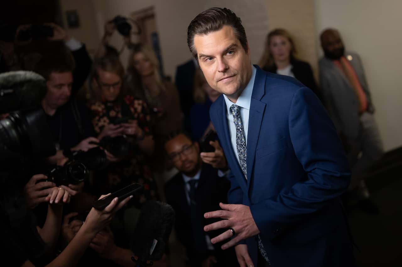 A man wearing a suit and tie speaking to journalists. 