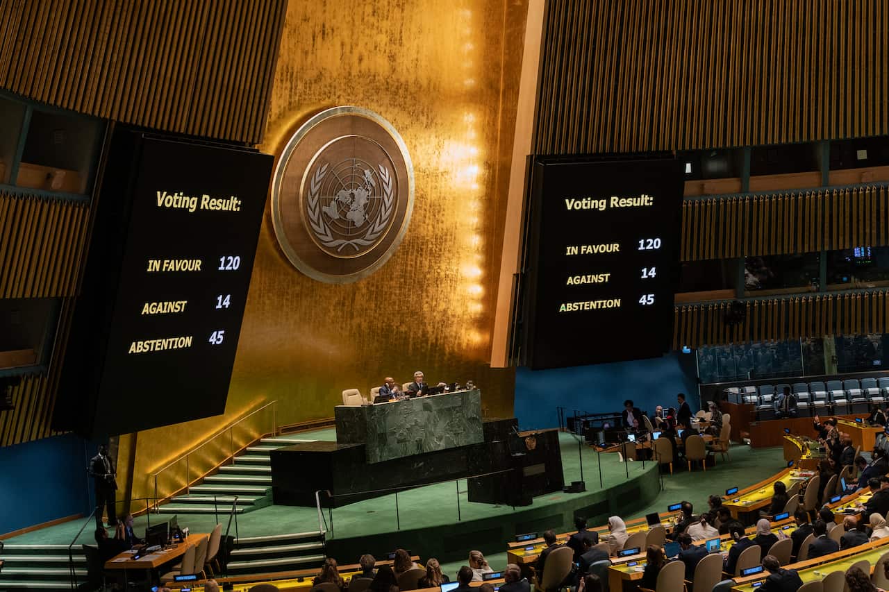 People sitting on podiums in a large room with the United Nations logo on the wall and big screens.