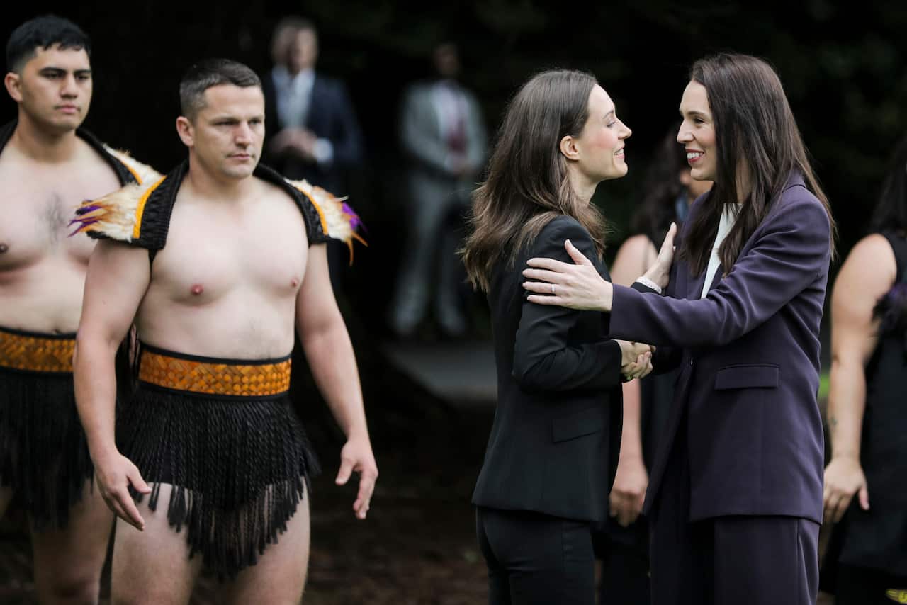 Finland's leader Sanna Marin (left) and New Zealand Prime Minister Jacinda Ardern (right) greeting each other beside men in traditional dress at Auckland Museum 