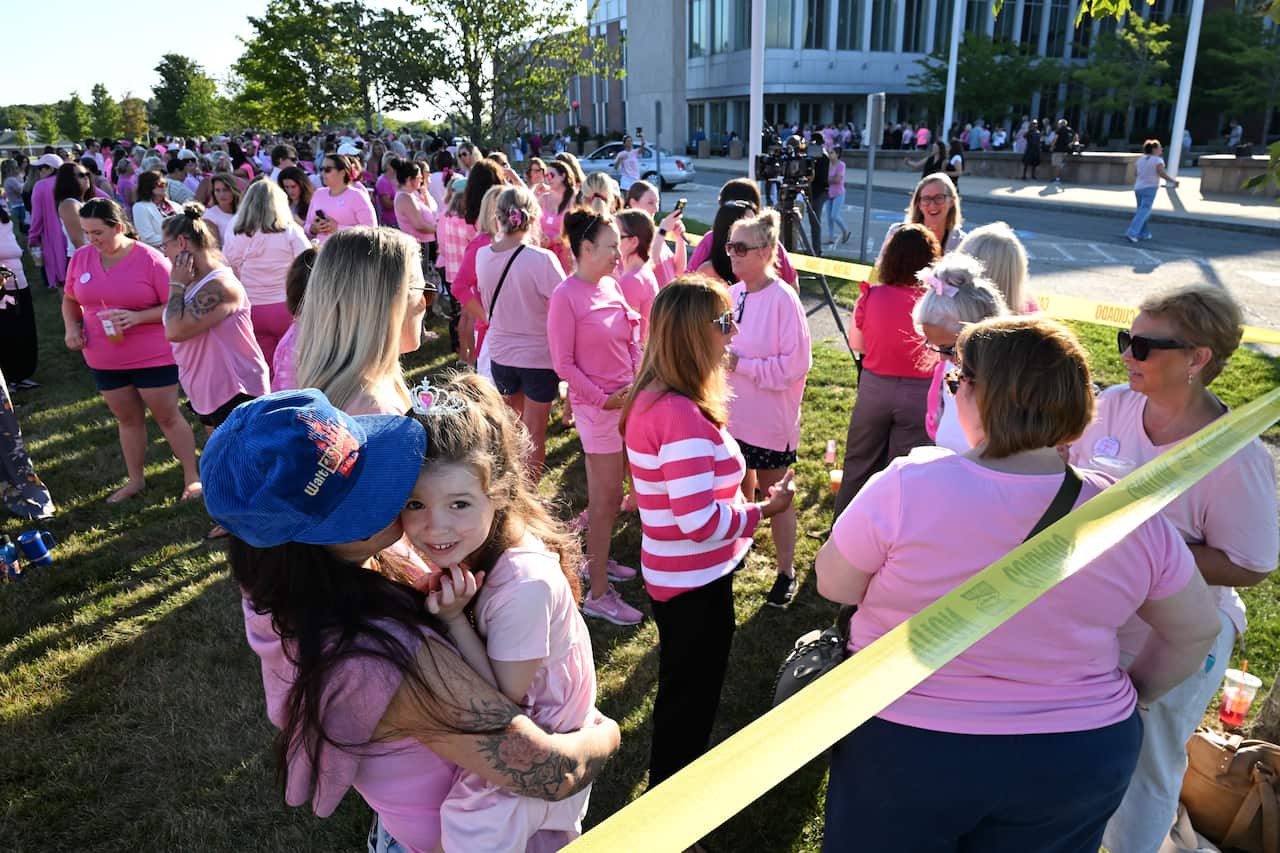 Women dressed in pink gather on a lawn outside an offiical building.