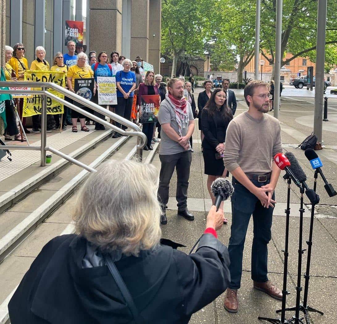 Man speaking at microphone with crowd of people standing behind him.