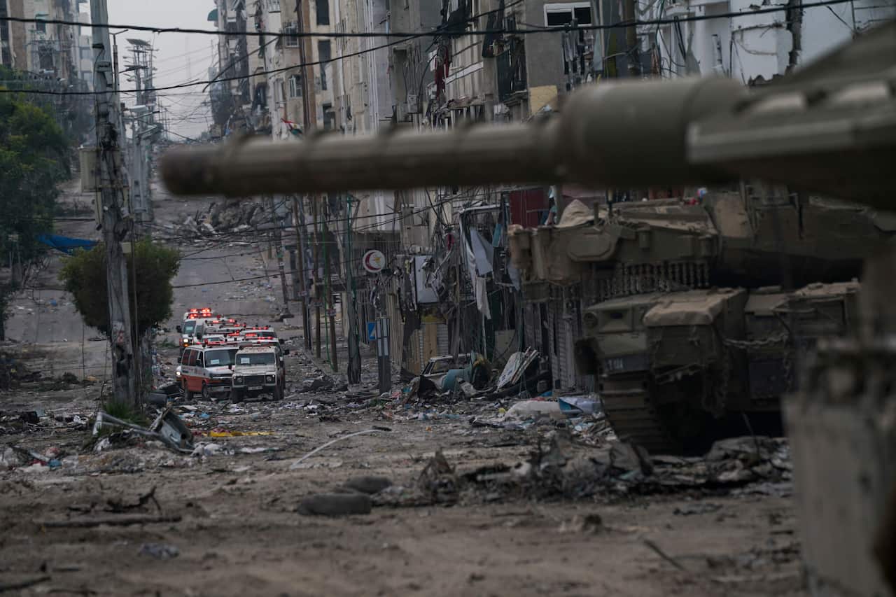 A tank in the foreground with ambulances in the background on a street strewn with debris.