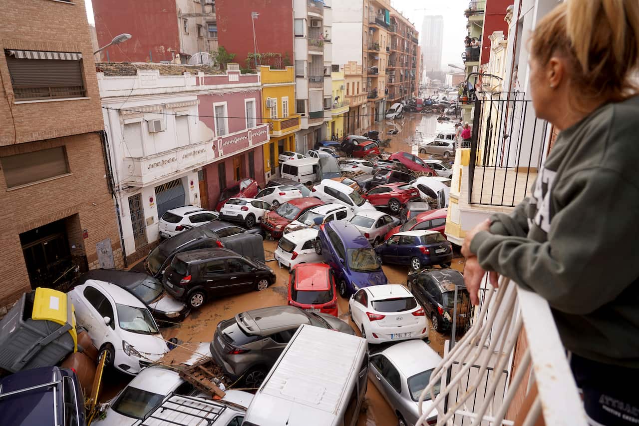 A woman looks out from her balcony on to a street filled with cars left there by floodwaters