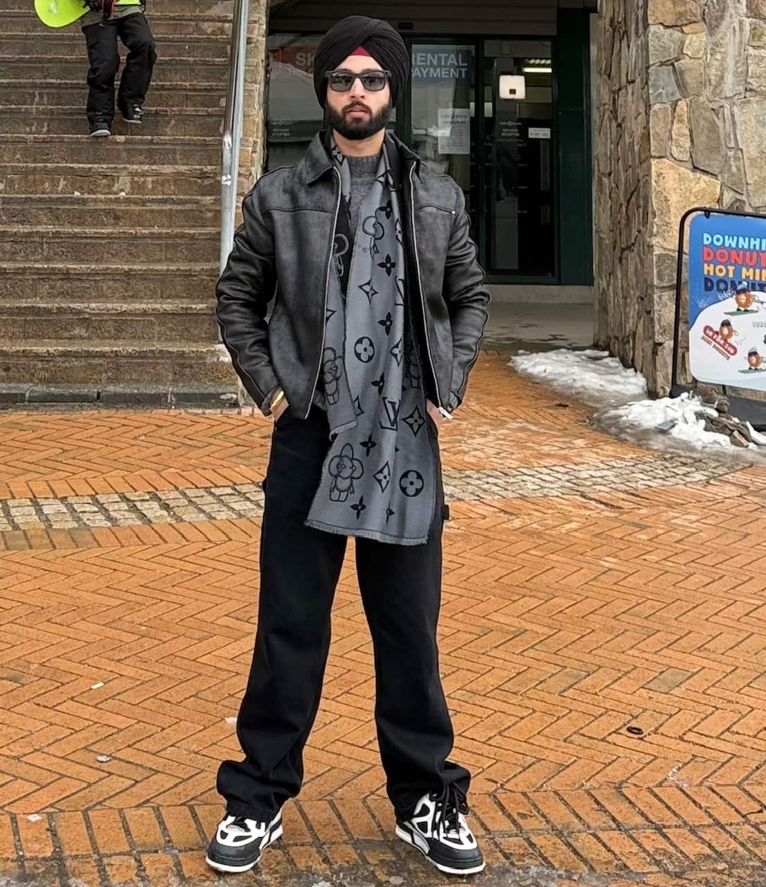 A man wearing a turban stands with his hands in his pockets and stares at the camera with a neutral expression on his face.