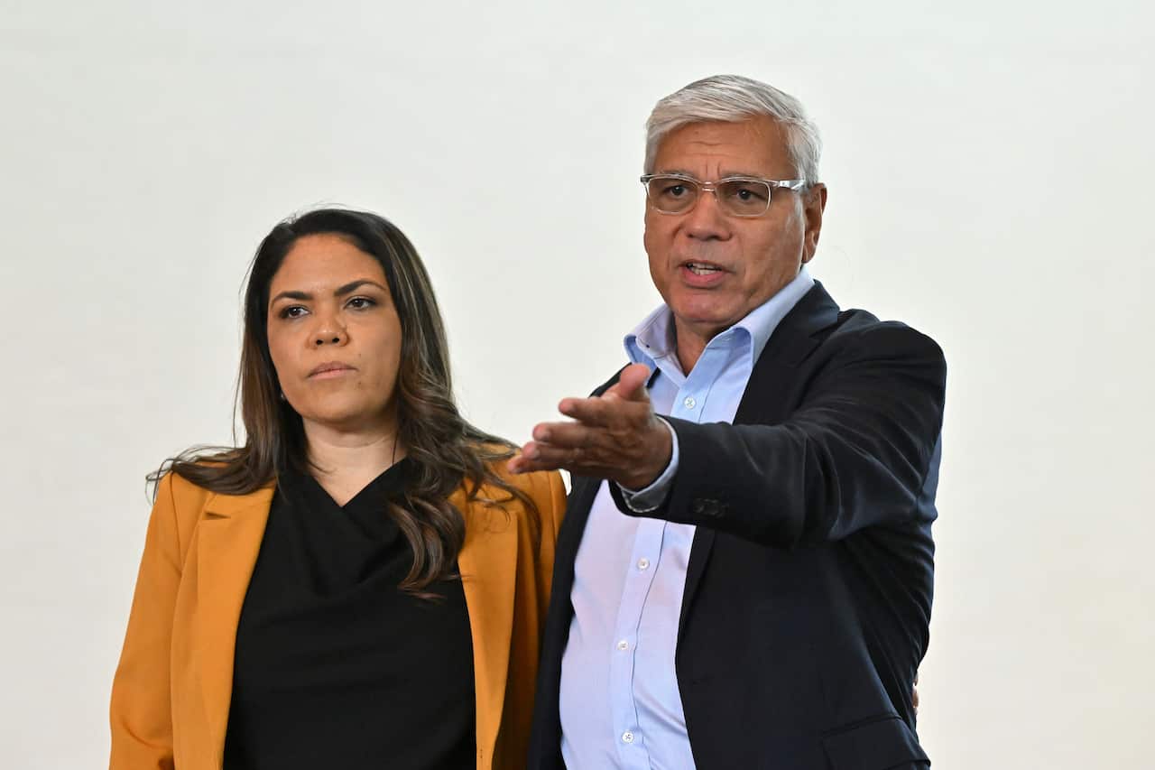 A woman and a man standing next to each other. The man is speaking and gesturing with his hand.
