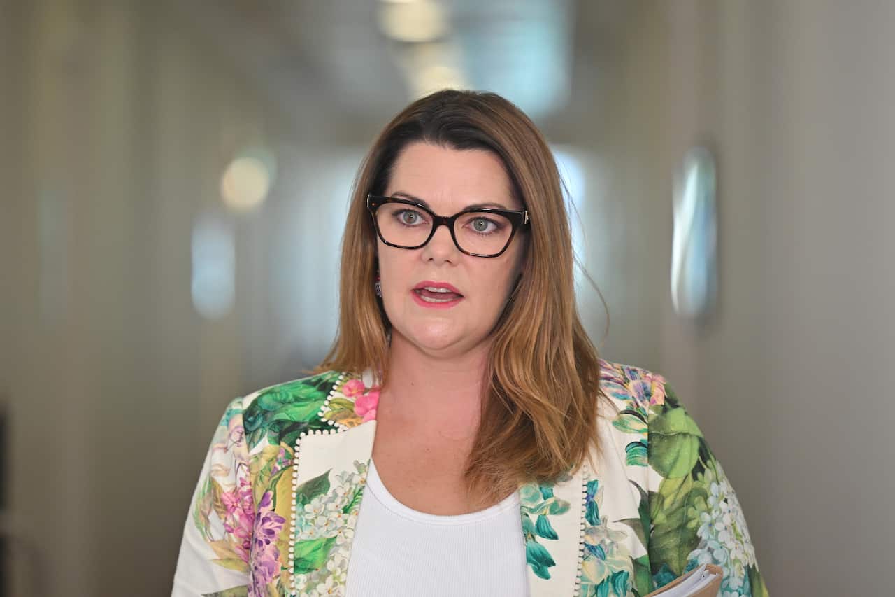 A woman in a floral blazer speaking in a hallway.