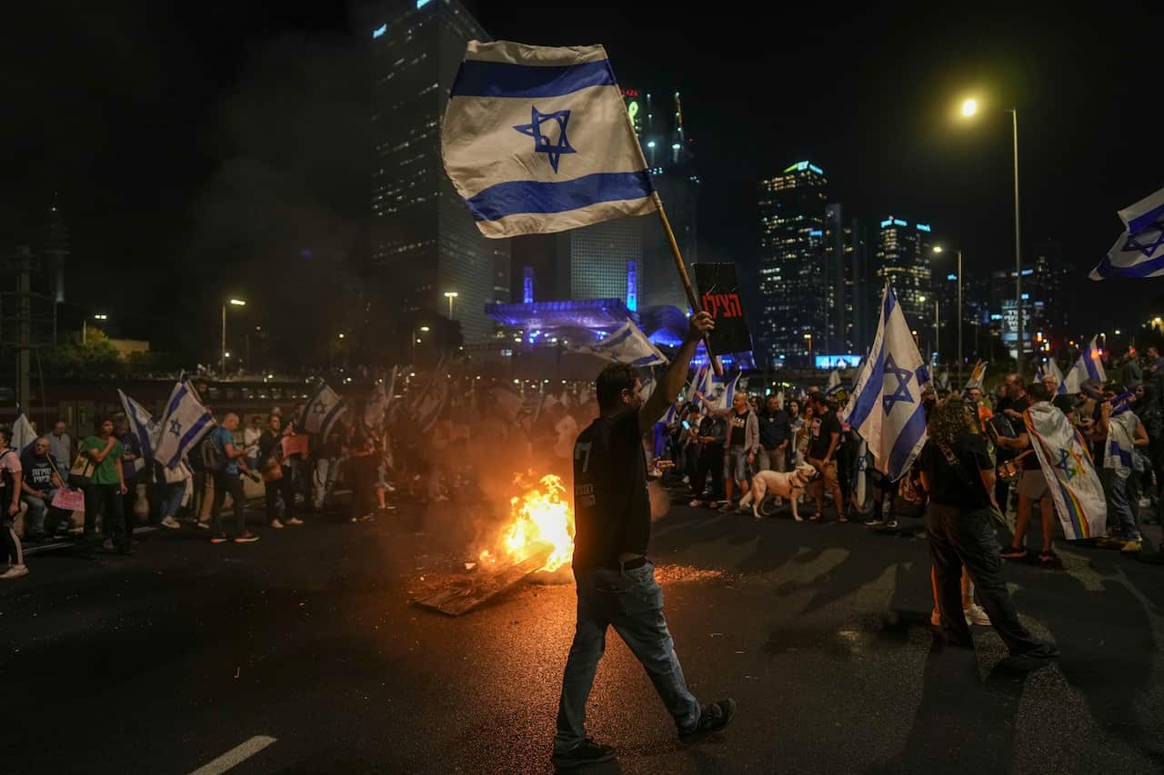 A group of people protesting in the middle of a street, many holding Israeli flags.