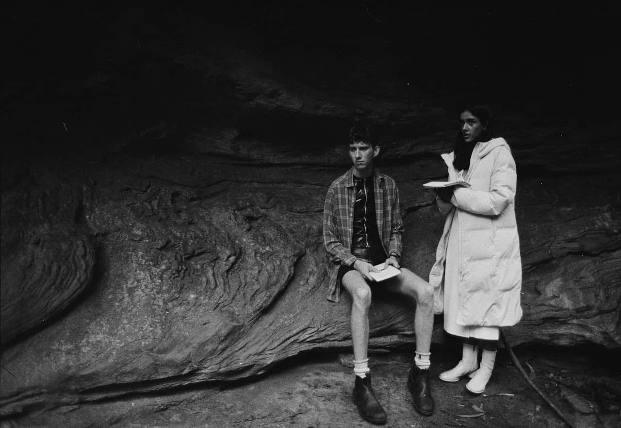 A man sits next to a woman who is standing