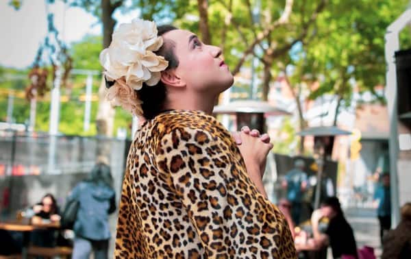A transgender woman with folded hands looking up.